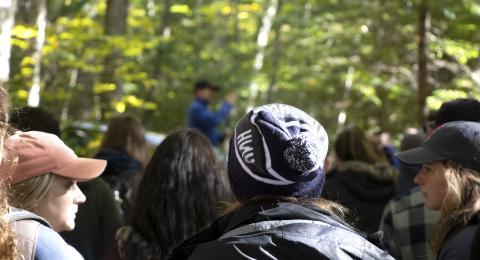 A crowd of students in the woods, one wearing a UNH beanie