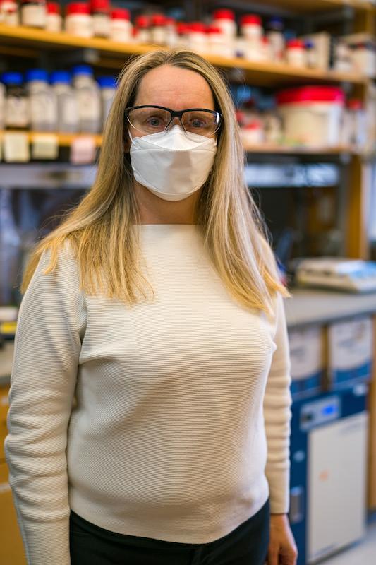 戴着口罩的女研究员站在实验室里看着镜头