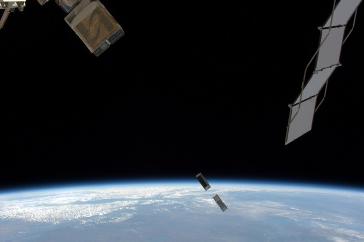 Tiny satellite floats above Earth in between much larger 空间科学 equipment.